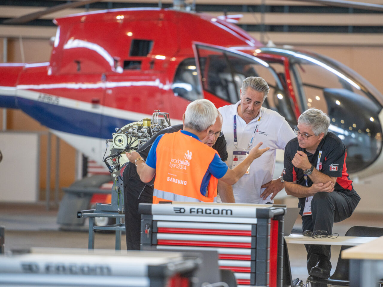 Experts at WorldSkills Lyon 2024 discuss the Aircraft Maintenance Competition in front of a helicopter.